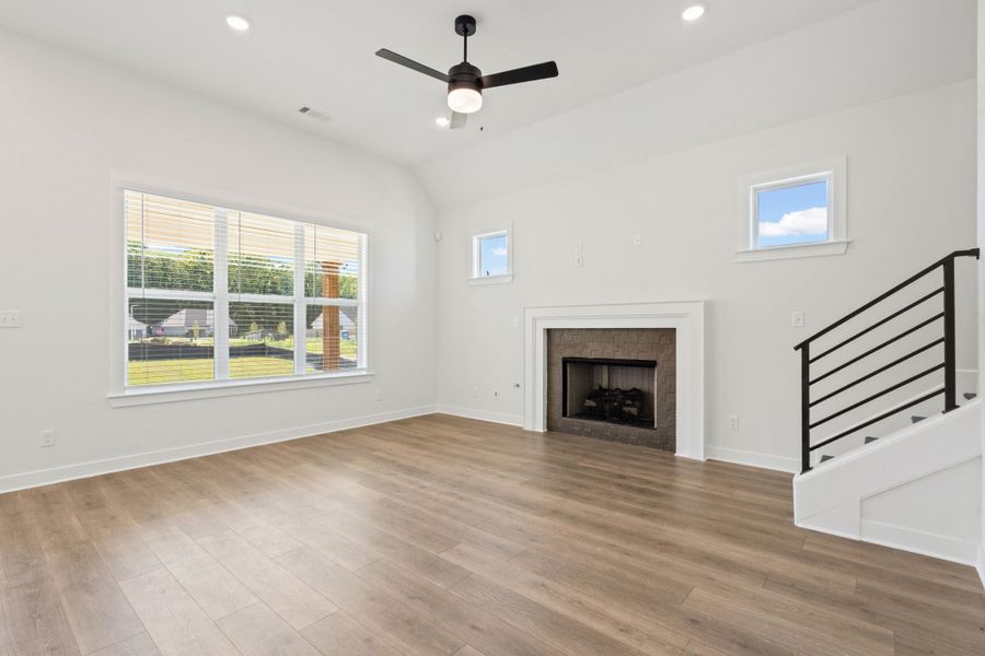 Vaulted ceiling featuring a ceiling fan and recessed lighting, wood-finish flooring, fireplace with stone surround and white mantel, and a staircase with a black metal railing Vaulted ceiling featuring a ceiling fan and recessed lighting, wood-finish flooring, fireplace with stone surround and white mantel, and a staircase with a black metal railing