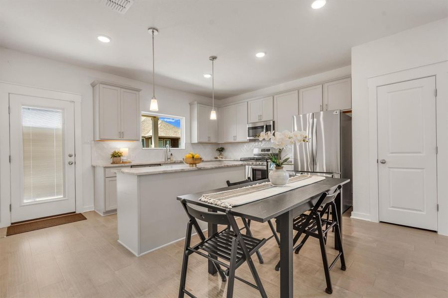 Bright, modern kitchen with sleek white cabinetry, stainless steel appliances, and a central island. Features recessed lighting, pendant lights, and a cozy dining area.