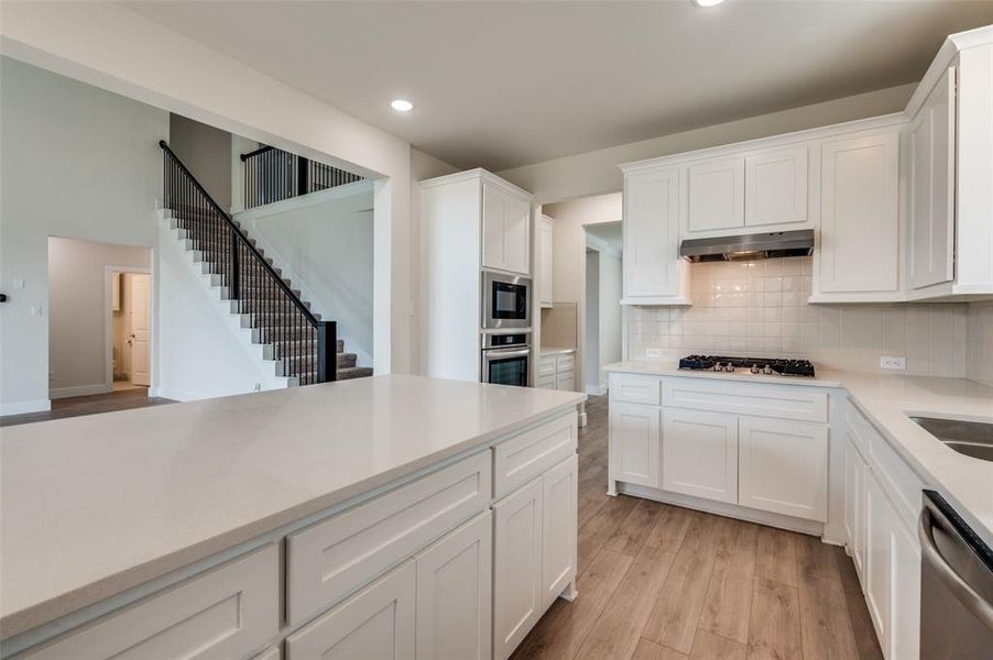 Kitchen with stainless steel appliances, light wood-type flooring, recessed lighting, under cabinet range hood, and tasteful backsplash Kitchen with stainless steel appliances, light wood-type flooring, recessed lighting, under cabinet range hood, and tasteful backsplash