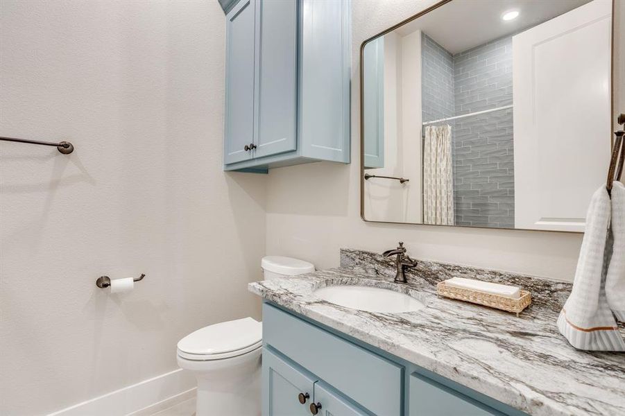 Bathroom featuring a light blue vanity, gray-patterned countertop, oil-rubbed bronze fixtures, and a shower with gray subway tile surround