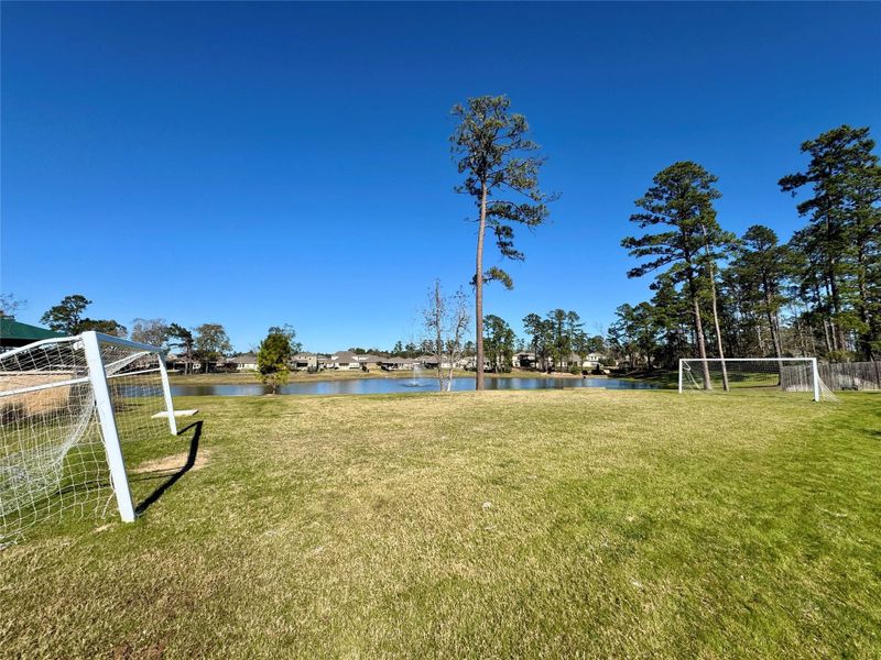 Grassy area featuring two soccer goals, surrounded by tall trees and a view of a serene pond, perfect for outdoor activities and sports. Grassy area featuring two soccer goals, surrounded by tall trees and a view of a serene pond, perfect for outdoor activities and sports.