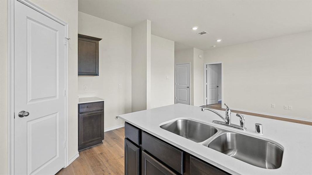 Kitchen featuring light wood finished floors, dark wood finish cabinetry, recessed lighting, and light stone countertops
