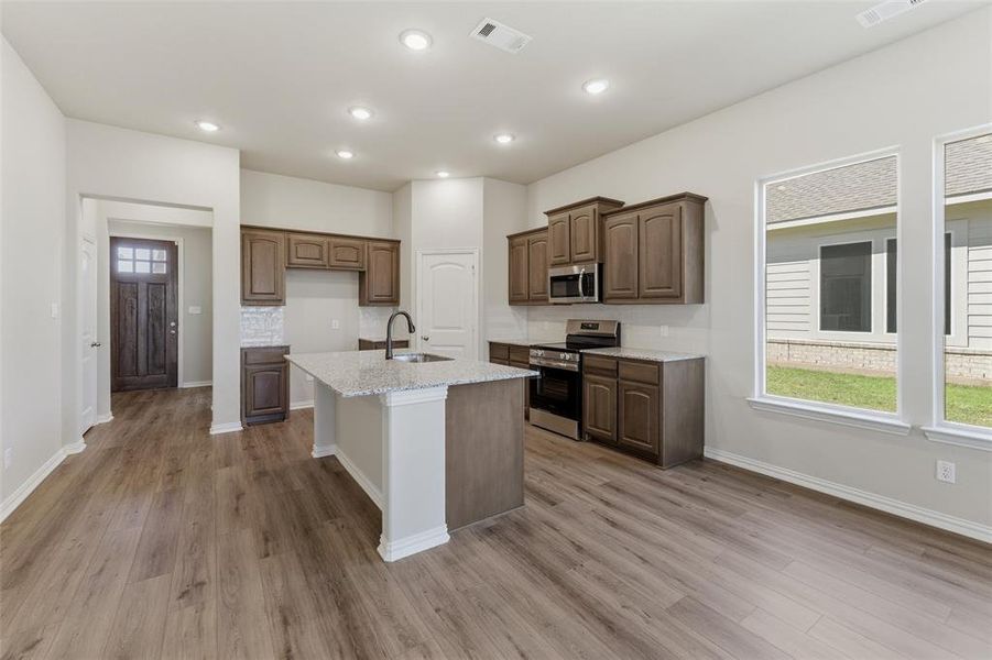 Kitchen featuring stainless steel appliances, light stone counters, a kitchen island with sink, light wood-type flooring, and recessed lighting