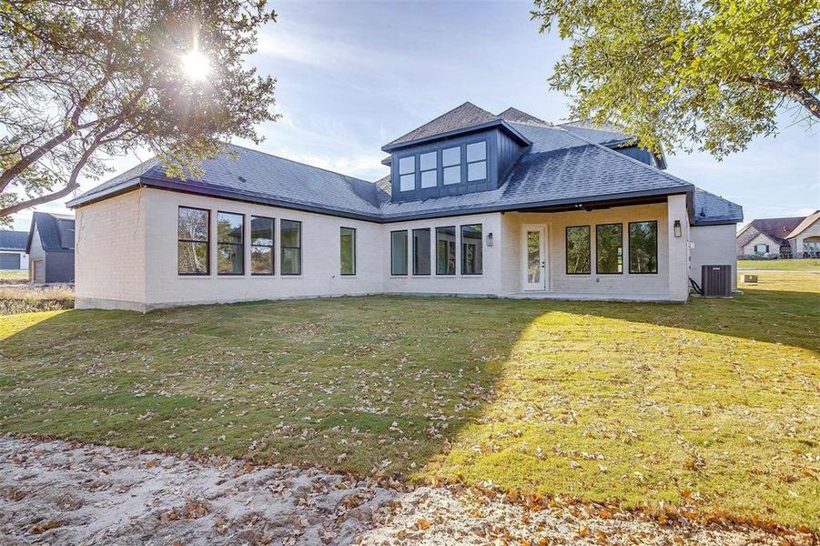 Back of property featuring central air condition unit, brick siding, a lawn, and roof with shingles Back of property featuring central air condition unit, brick siding, a lawn, and roof with shingles