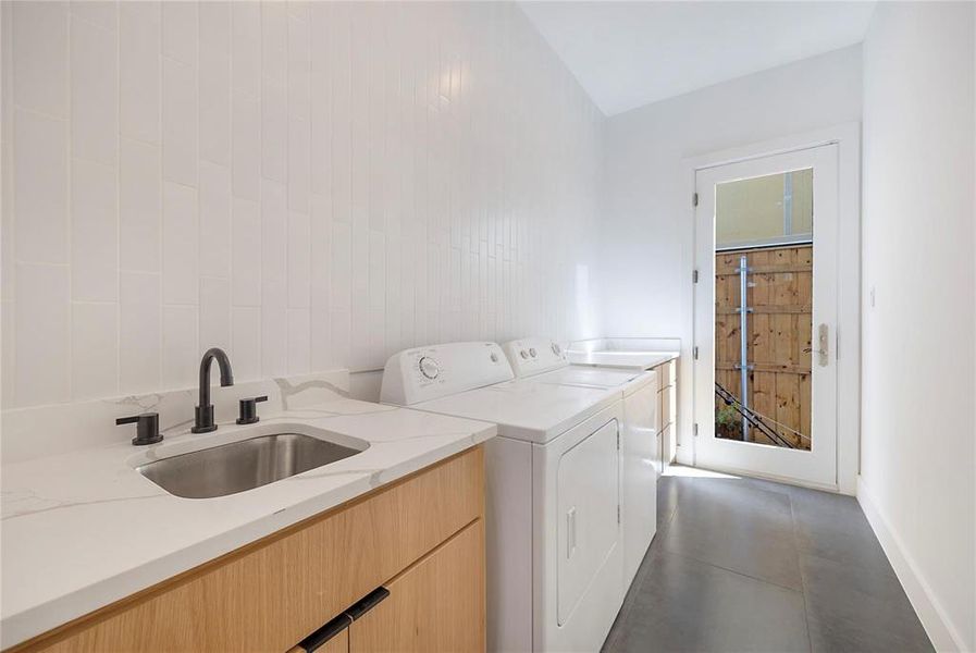 Laundry area featuring dark tile patterned floors, sink, washing machine and clothes dryer, and cabinets