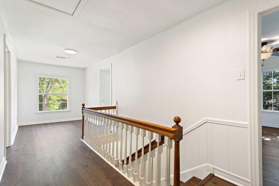 Hall featuring an upstairs landing, plenty of natural light, dark wood finished floors, and a wainscoted wall