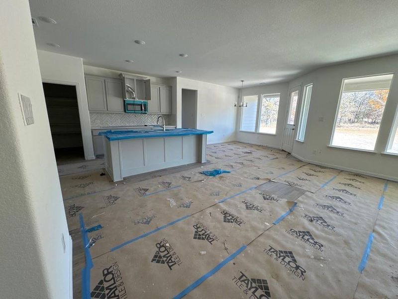 Kitchen with gray cabinets, stainless steel microwave, tasteful backsplash, a kitchen island with sink, and a chandelier