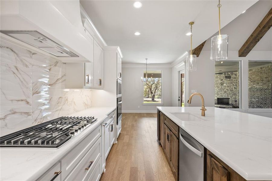 Two tone kitchen with two tone cabinetry, pendant lighting, light wood-type flooring, stainless steel appliances, and beam ceiling