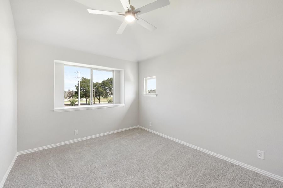 Empty bedroom with carpet flooring, ceiling fan, and two windows with outdoor views