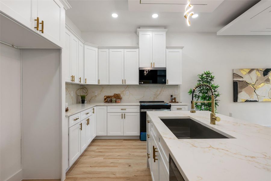 Kitchen featuring white cabinets, black appliances, light stone counters, light wood finished floors, and decorative backsplash Kitchen featuring white cabinets, black appliances, light stone counters, light wood finished floors, and decorative backsplash