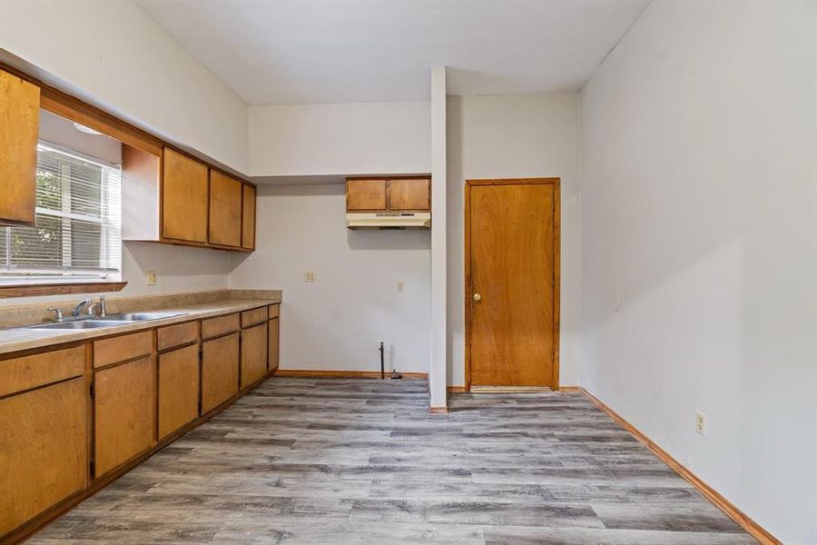 Kitchen featuring light wood finished floors, light countertops, brown cabinetry, and under cabinet range hood Kitchen featuring light wood finished floors, light countertops, brown cabinetry, and under cabinet range hood