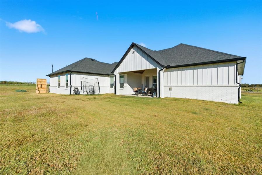 Rear view of house with board and batten siding, a yard, a patio, and roof with shingles