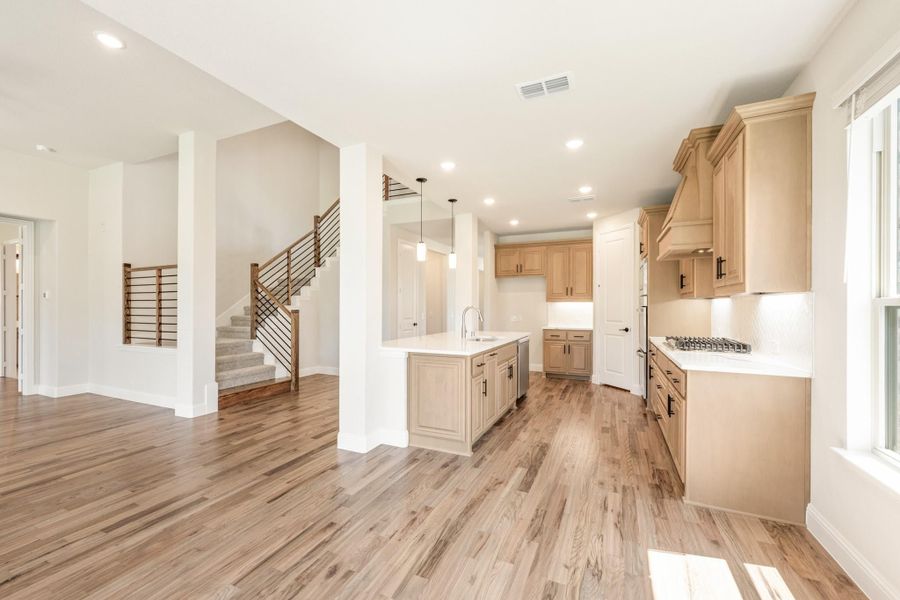 Open kitchen with light wood cabinets, center island, and hardwood floors, open to staircase and living area Open kitchen with light wood cabinets, center island, and hardwood floors, open to staircase and living area