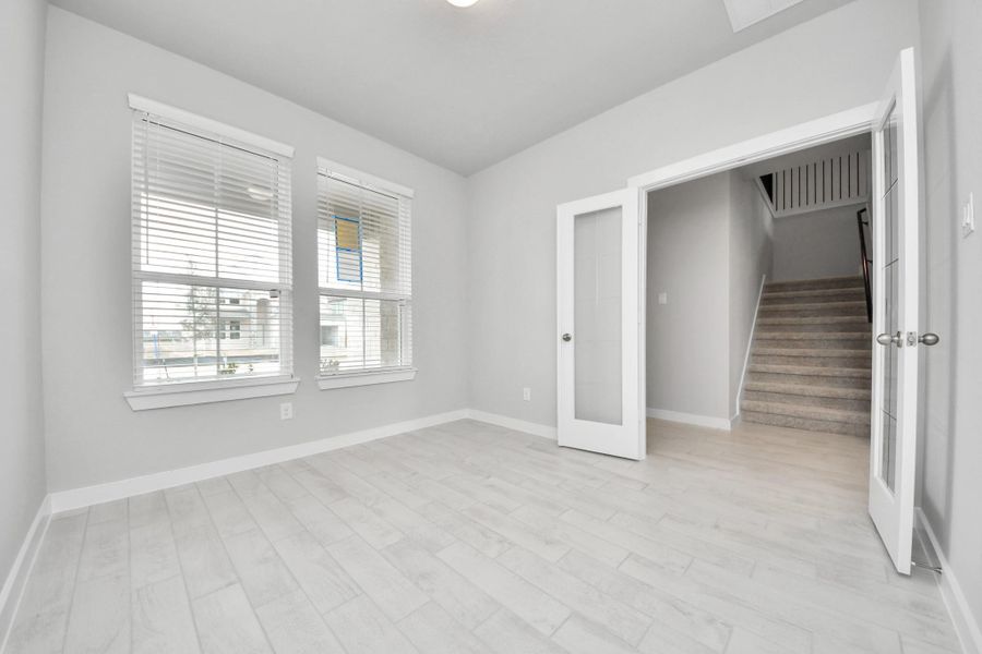 Experience the perfect blend of sophistication and warmth in this home office, boasting elegant wood-look tile flooring and flooded with natural light from expansive windows and French doors. Sample photo of completed home with similar floor plan. Actual colors and selections may vary.