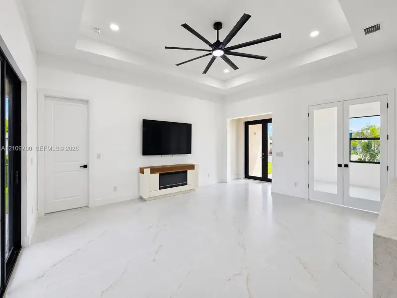 Tray ceiling with recessed lighting, large-format tile flooring, multi-blade ceiling fan, built-in electric fireplace, and French doors