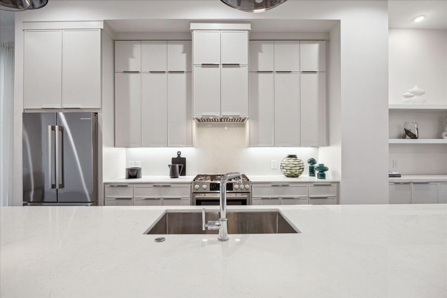 Symmetrical kitchen wall showcasing full-height cabinetry and a centered cooking area beneath a streamlined vent hood. Soft integrated lighting highlights the smooth backsplash and refined finishes. The cohesive design, paired with crisp lines and balanced proportions, creates a polished, modern aesthetic that complements the open-concept main level.
