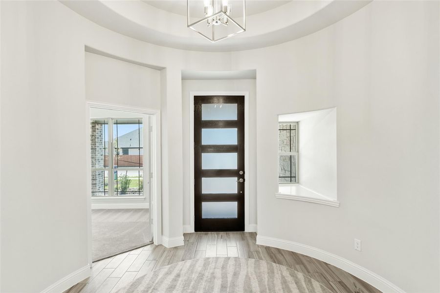 Curved entryway with dark wood front door, tray ceiling, chandelier, and light hardwood floors