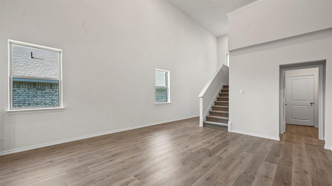 Vaulted ceiling living area featuring wood-finish flooring, white trim, and a carpeted staircase with white railings
