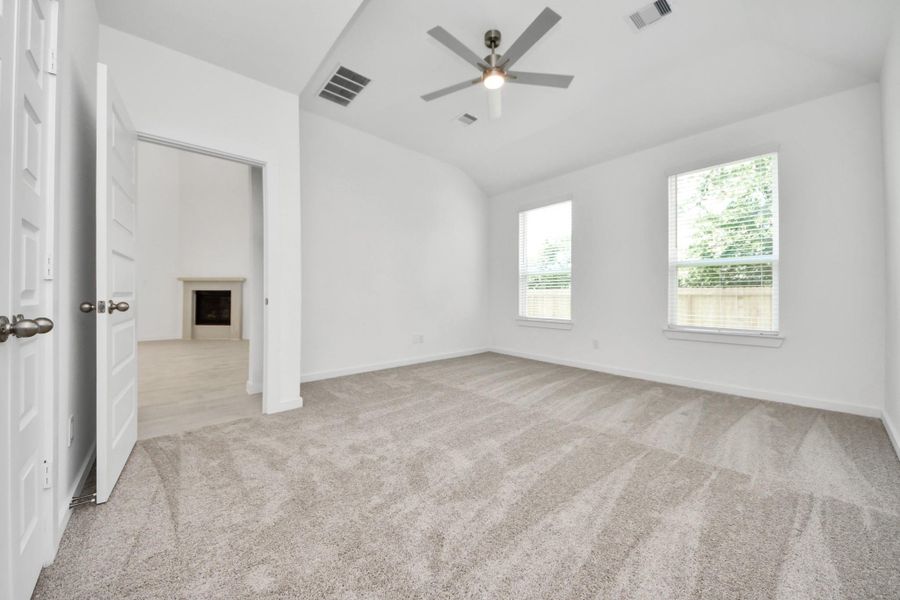 Escape and relax in the exquisite primary suite, a haven to unwind after a long day. The spacious room, located on first floor, boasts plush carpeting, soothing paint tones, high ceilings, and expansive windows adorned with privacy blinds. Sample photo of completed home with similar floor plan. Actual colors and selections may vary.