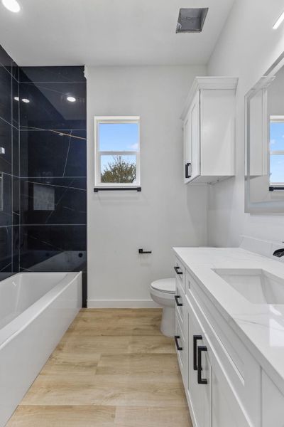 Gleaming stone counters and sleek tiled walls define this modern, light-filled bathroom.