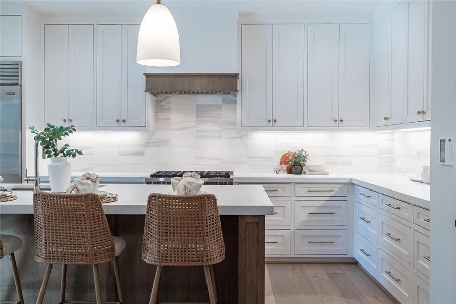 Kitchen with decorative backsplash, white cabinets, a kitchen bar, light hardwood / wood-style flooring, and pendant lighting