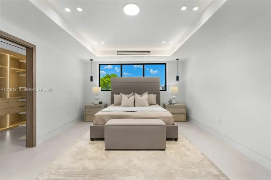 Tray ceiling with recessed lighting, integrated accent lighting, large windows with black frames, and a walk-in closet with built-in storage shelving Tray ceiling with recessed lighting, integrated accent lighting, large windows with black frames, and a walk-in closet with built-in storage shelving
