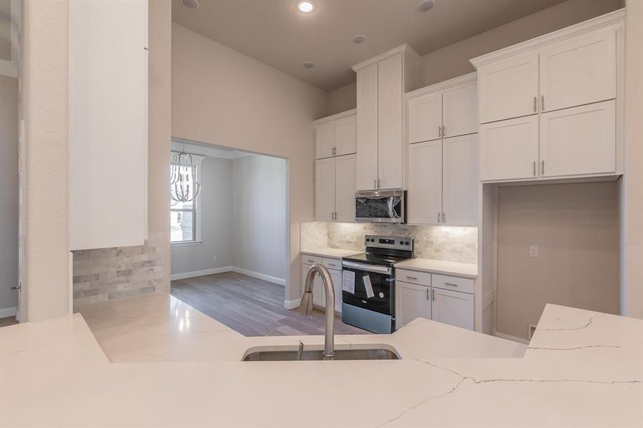 Kitchen with decorative backsplash, stainless steel appliances, sink, white cabinets, and light hardwood / wood-style floors