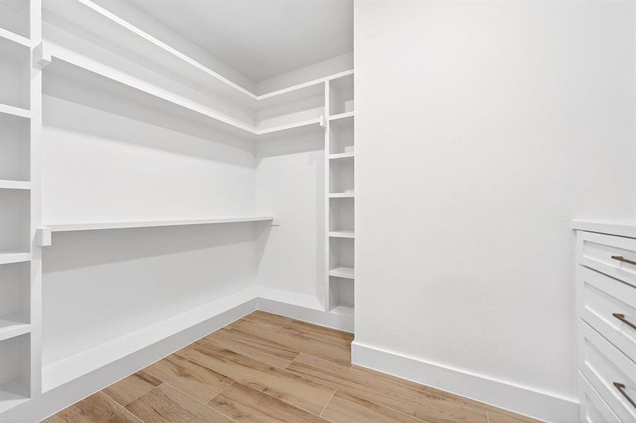 Walk-in closet with built-in shelving, vertical storage compartments, wood-finish tile flooring, white baseboards, and a built-in dresser with bronze hardware Walk-in closet with built-in shelving, vertical storage compartments, wood-finish tile flooring, white baseboards, and a built-in dresser with bronze hardware