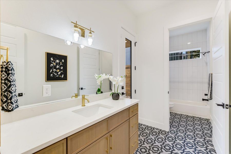 The secondary bathroom steals the show with its striking geometric floor tile and gold-finished fixtures, offering a playful yet sophisticated vibe that is quintessentially East Austin.