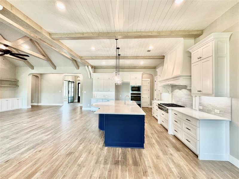 Kitchen featuring a kitchen island with sink, hanging light fixtures, white cabinetry, ceiling fan, and light wood-type flooring