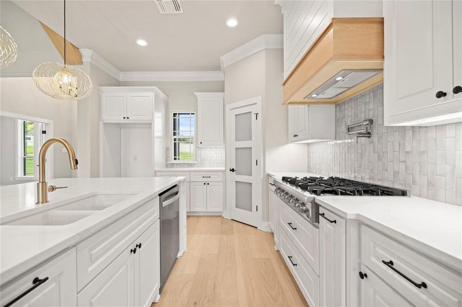Kitchen with backsplash, ornamental molding, white cabinetry, stainless steel appliances, and light wood finished floors Kitchen with backsplash, ornamental molding, white cabinetry, stainless steel appliances, and light wood finished floors