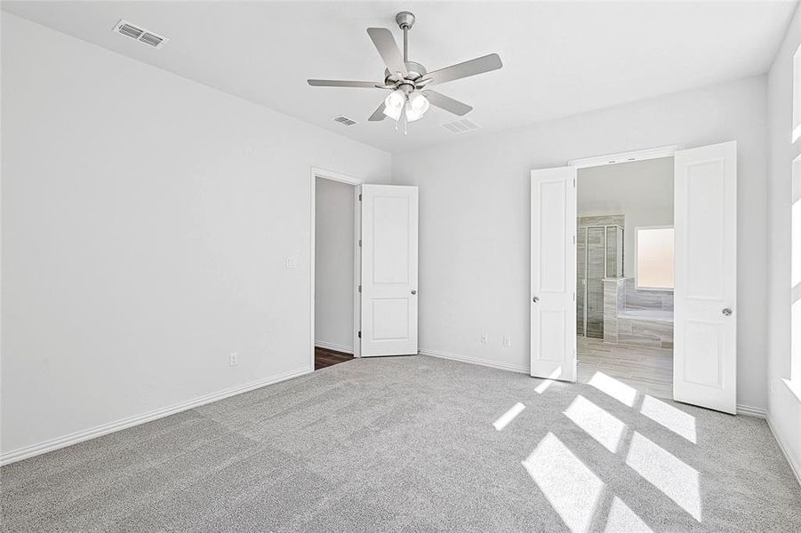 Unfurnished bedroom featuring ceiling fan, light colored carpet, and ensuite bath