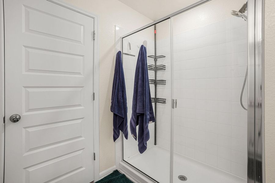 A well-appointed shower stall features clean white tile and convenient built-in shelving.