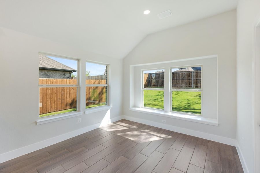 Empty room with vaulted ceiling, wood-look tile floors, and large windows overlooking a backyard Empty room with vaulted ceiling, wood-look tile floors, and large windows overlooking a backyard