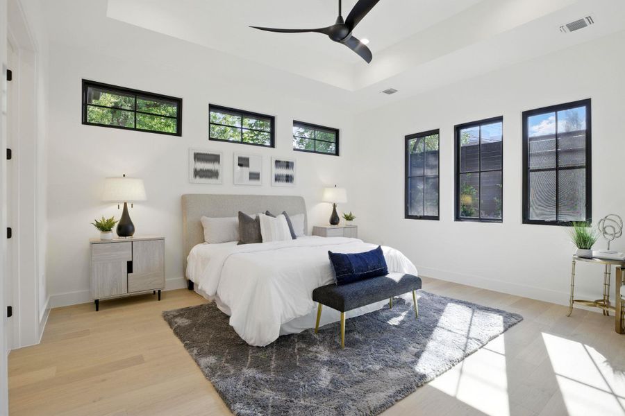 Bedroom featuring a raised ceiling, light wood-style floors, baseboards, and a ceiling fan