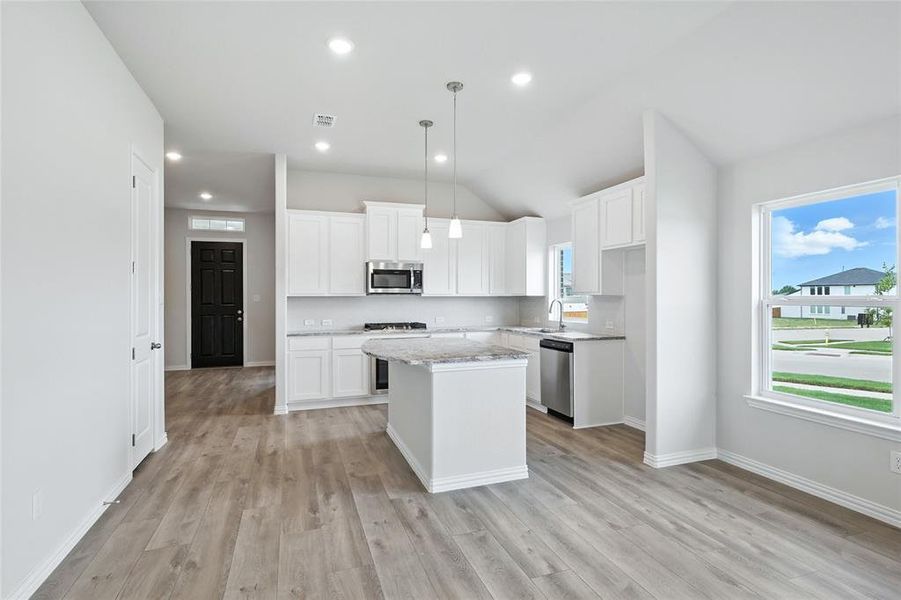 Kitchen featuring stainless steel appliances, vaulted ceiling, a center island, light wood finished floors, and white cabinets
