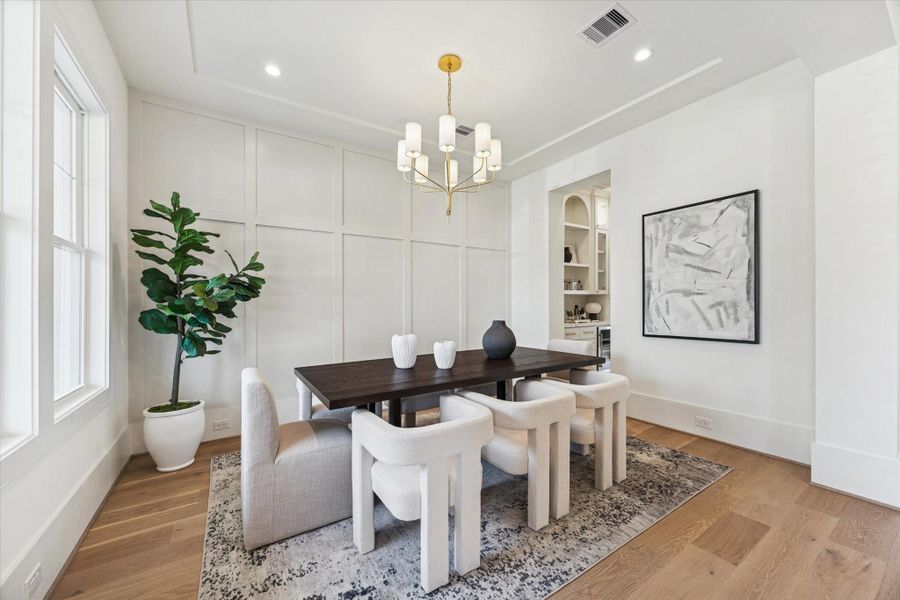 Elegant dining room with a statement chandelier, natural light, and clean wall detailing that creates a warm, elevated atmosphere.