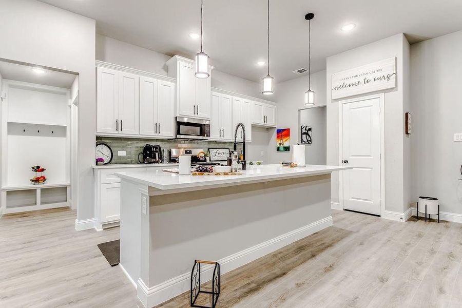 Kitchen with stainless steel appliances, white cabinetry, hanging light fixtures, and an island with sink