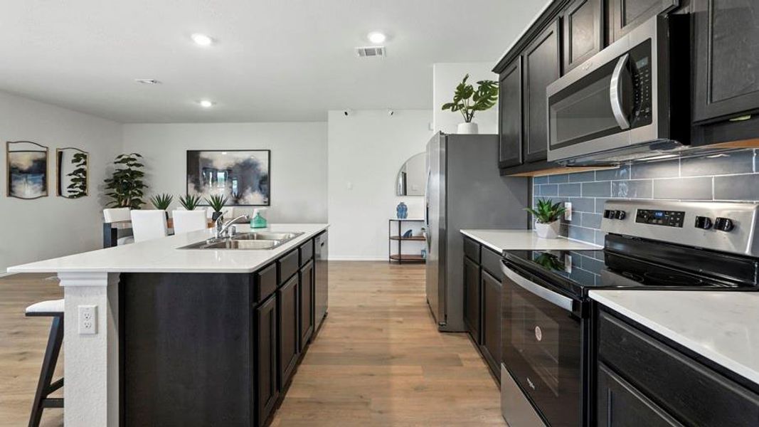 Kitchen featuring stainless steel appliances, a kitchen bar, an island with sink, light wood-style flooring, and tasteful backsplash Kitchen featuring stainless steel appliances, a kitchen bar, an island with sink, light wood-style flooring, and tasteful backsplash