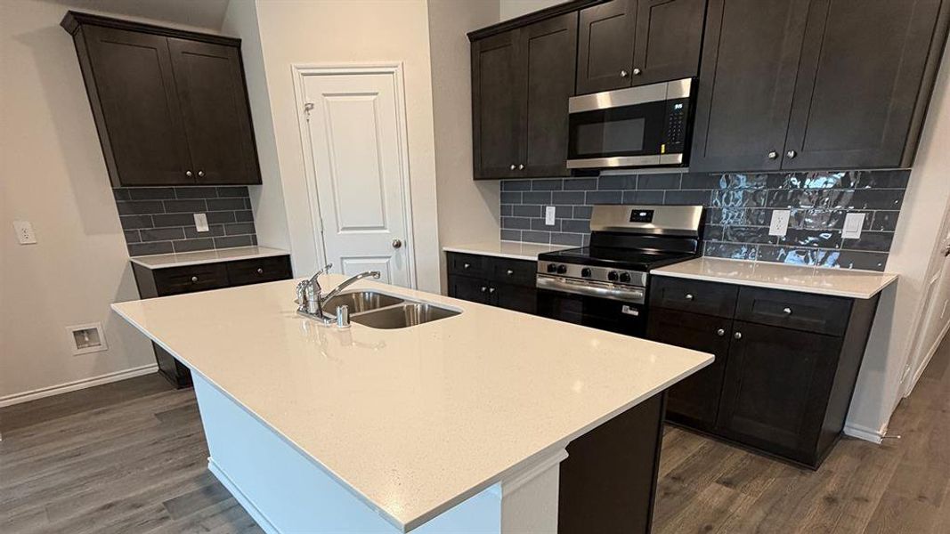 Kitchen featuring stainless steel appliances, tasteful backsplash, light stone countertops, and an island with sink