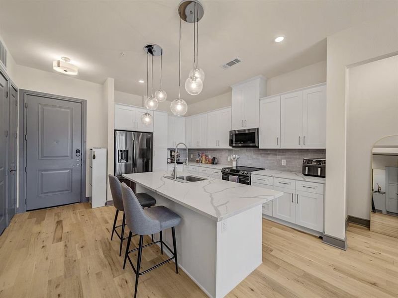 Kitchen with white cabinetry, appliances with stainless steel finishes, a breakfast bar, decorative backsplash, and decorative light fixtures Kitchen with white cabinetry, appliances with stainless steel finishes, a breakfast bar, decorative backsplash, and decorative light fixtures