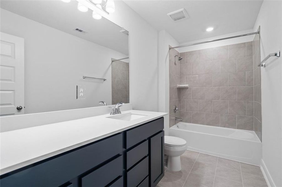 Secondary bath features tile flooring, tub/shower combo with tile surround, stained wood cabinets, beautiful light countertops, mirror, sleek fixtures and modern finishes.