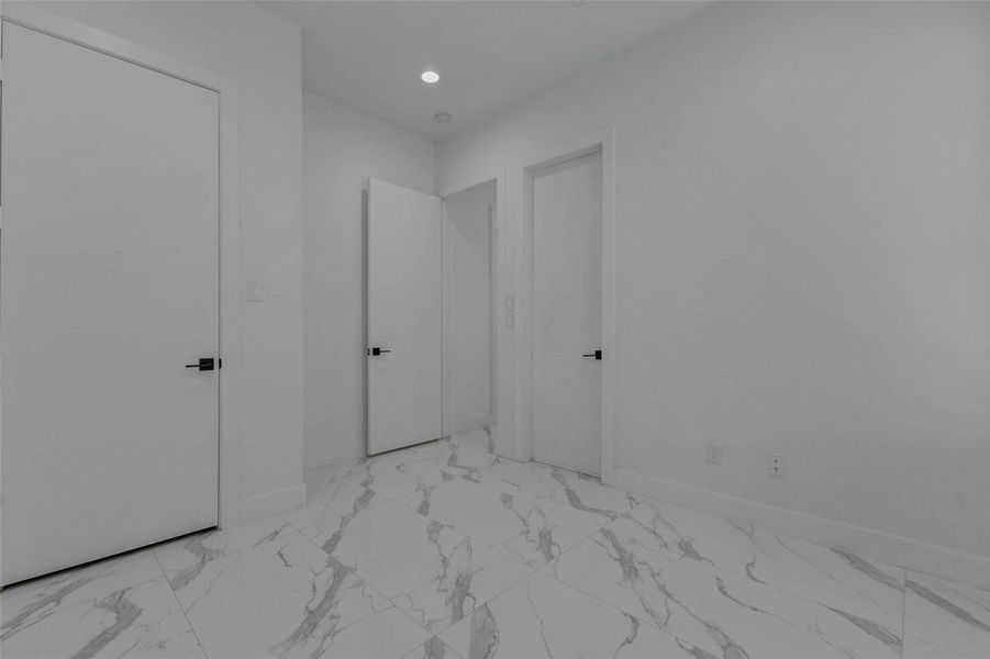 The second downstairs bedroom is finished with light walls, recessed lighting, marble-look tile flooring, window blinds, and a comfortable rectangular footprint. Its neutral design provides an easy foundation for furniture, artwork, and personal style.