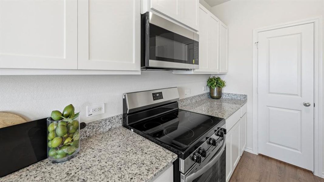 Kitchen featuring stainless steel appliances, white cabinets, light stone counters, and dark wood-style flooring Kitchen featuring stainless steel appliances, white cabinets, light stone counters, and dark wood-style flooring