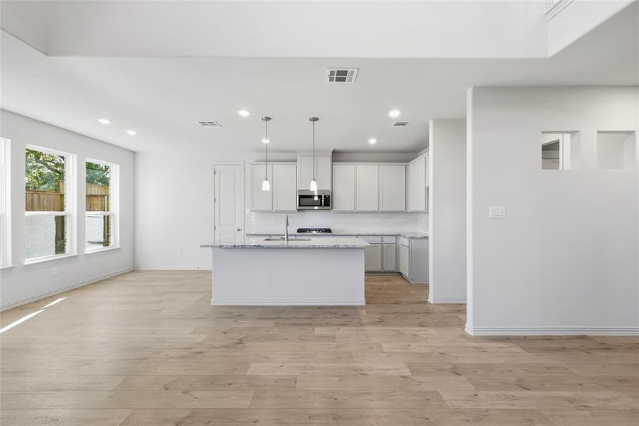 Kitchen featuring a center island with sink, hanging light fixtures, recessed lighting, white cabinetry, and light stone countertops
