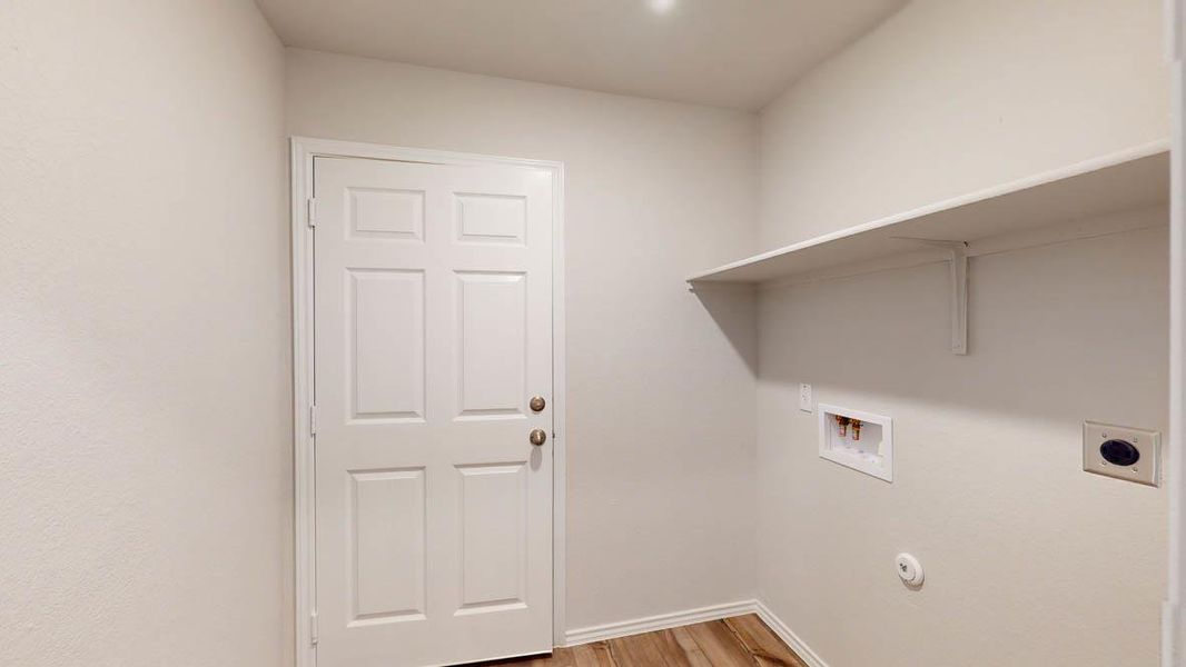 Dedicated utility space featuring wood-finish flooring, a six-panel interior door, a built-in wall shelf, and washer/dryer hookups