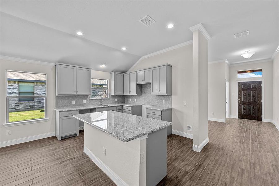 Kitchen featuring lofted ceiling, a kitchen island, hardwood / wood-style floors, gray cabinets, and light stone counters