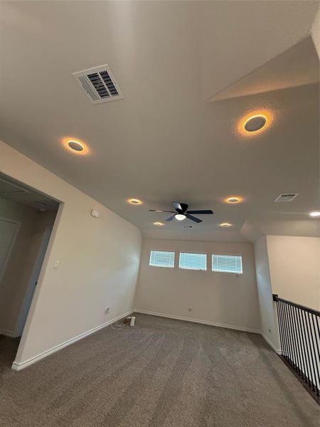 Spacious room featuring neutral carpeting, a ceiling fan, recessed lighting, and three high windows with horizontal blinds