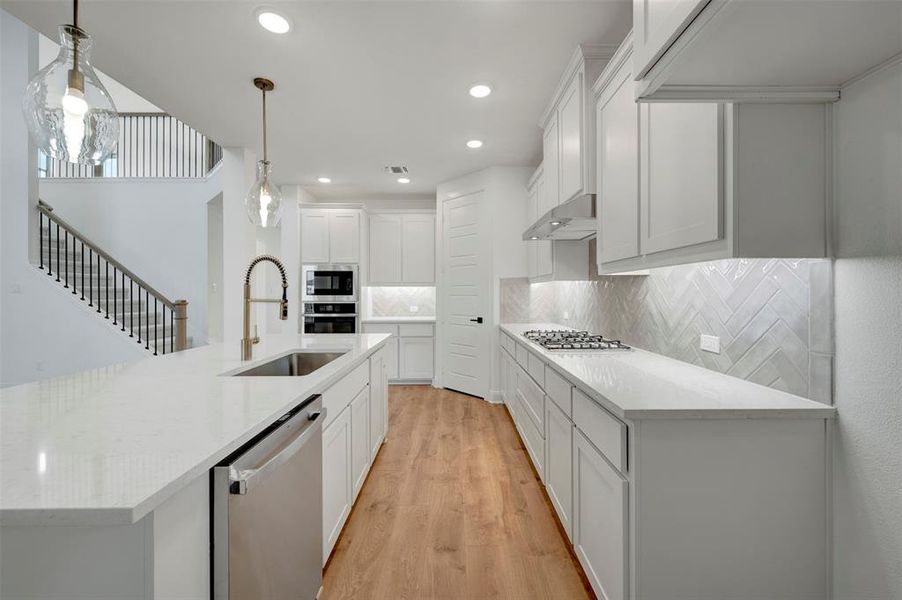 Kitchen featuring stainless steel appliances, white cabinets, an island with sink, and light stone counters