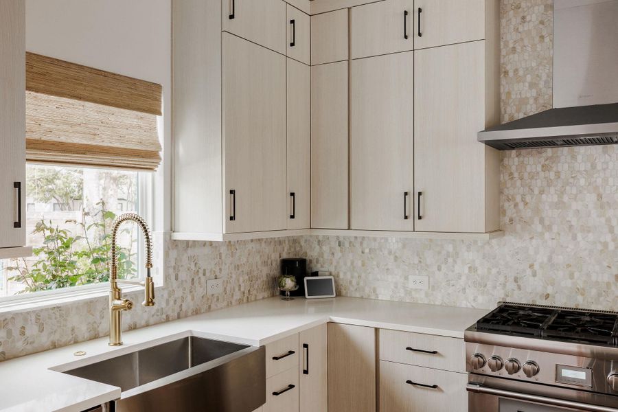 Kitchen featuring high end range, light wood finish cabinetry, light stone countertops, and tasteful backsplash
